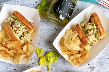 Overhead view of four plated Mini Shrimp Rolls with potato chips and a jar of pickled jalepenos.