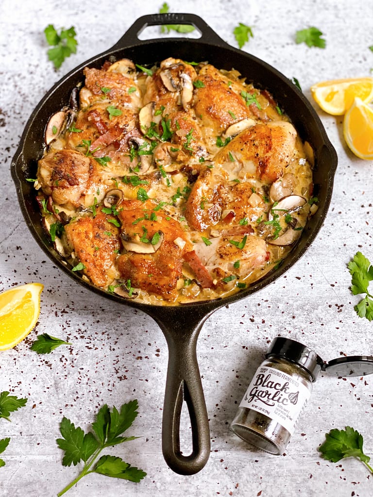 A skillet full of Black Garlic Chicken in a cream-based mustard sauce with mushrooms and parsley.