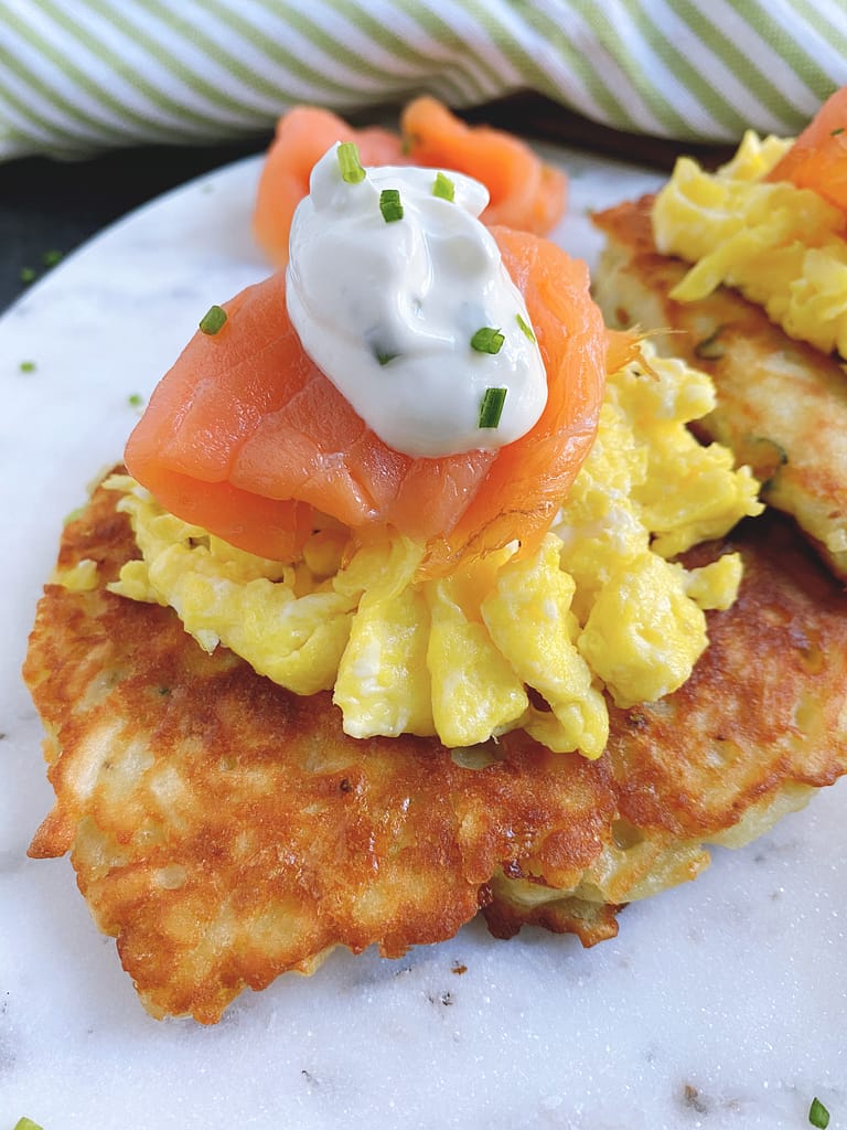 A closeup of the Potato Cakes with Scrambled Eggs and Smoked Salmon. The Potato Cake is the base, Scrambled Eggs are next. Then is the Smoked Salmon. It's topped with sour cream and chives for garnish.