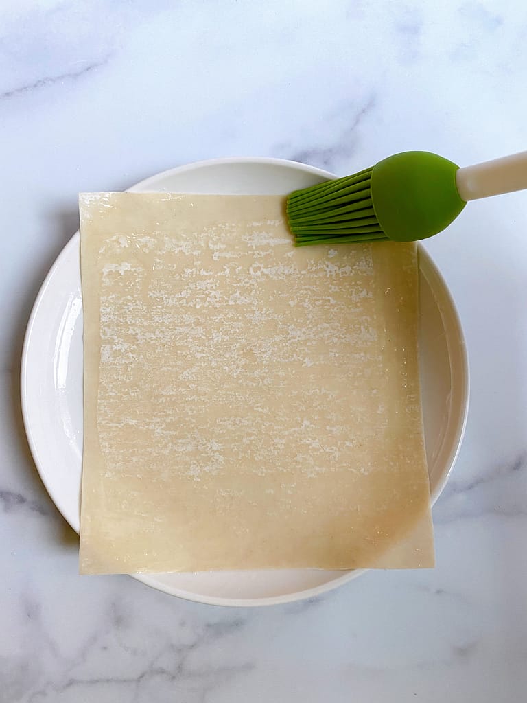 Brushing egg wash along the edges of the egg roll wrapper
