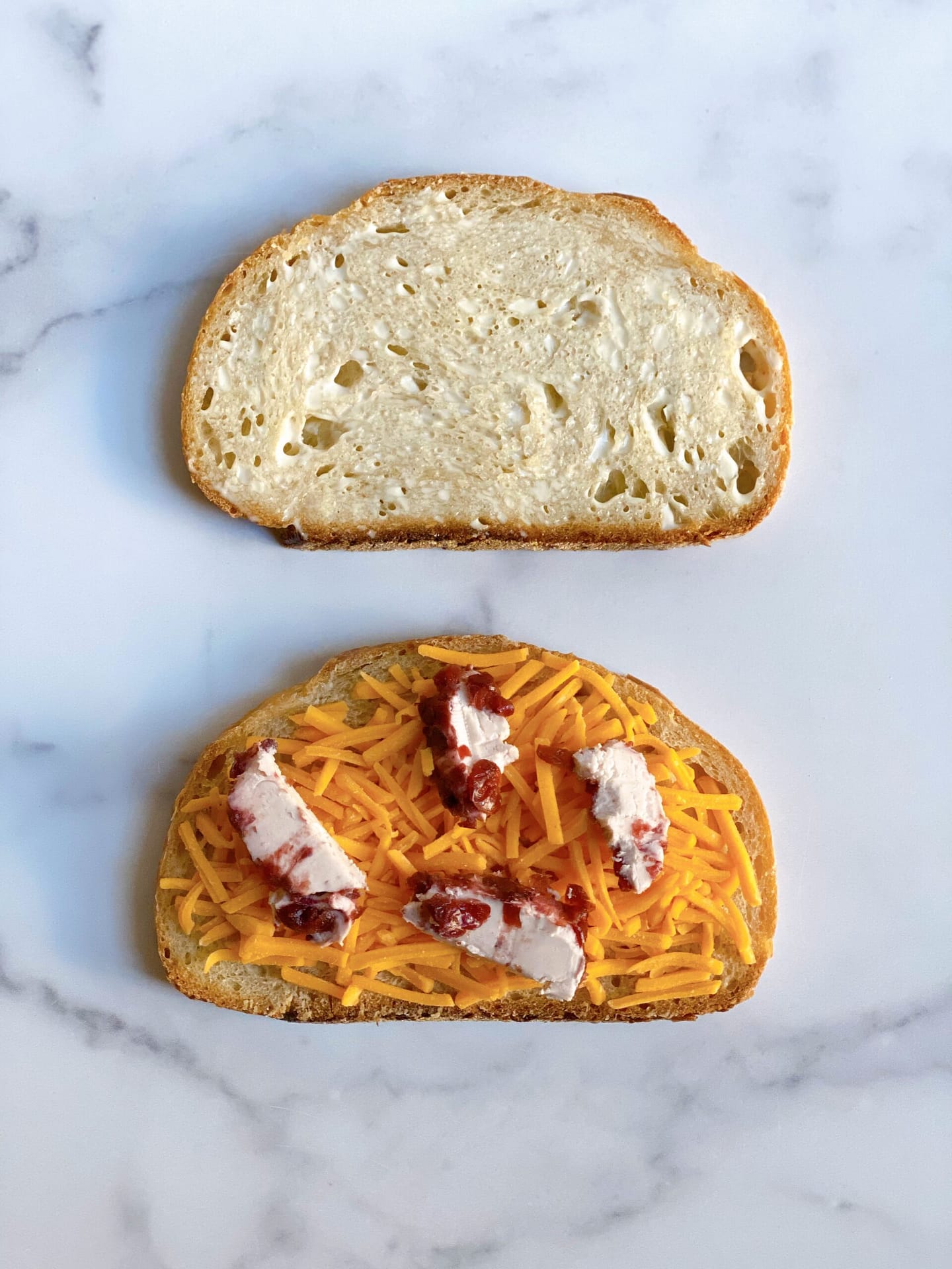 Two slices of sourdough bread. The first has mayo slathered on it. The second has sharp cheddar and cranberry goat cheese.