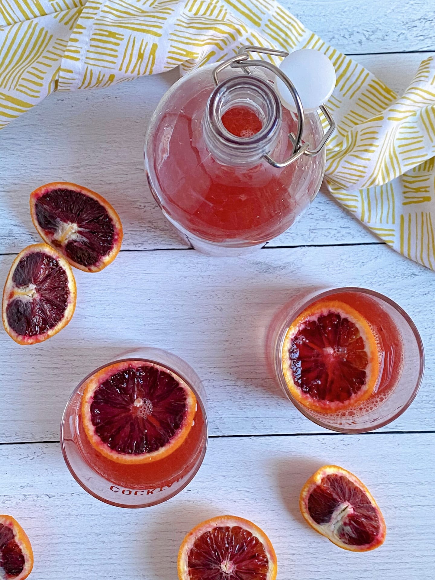 Overhead view of a pitcher of blood orange juice, two glasses of sparkling blood orange cooler and assorted slice of blood orange